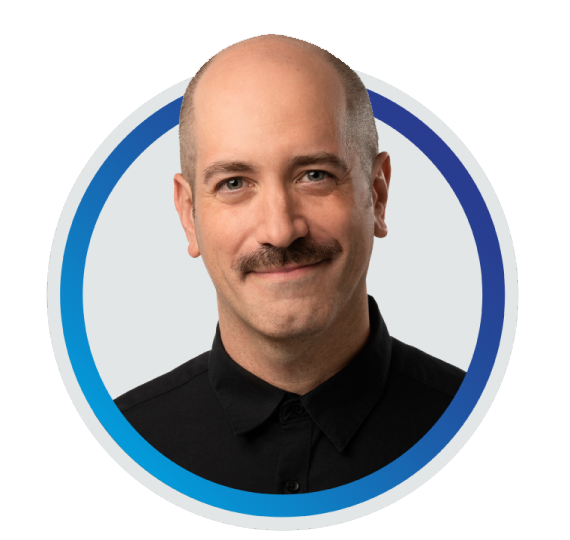 Thomas Logan, a man with light skin and a bald head smiles gently at the camera. He has a dark mustache and wears a black collared shirt buttoned to the top. He appears professional and approachable.